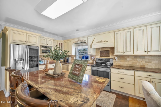 kitchen featuring a skylight, dark stone counters, cream cabinets, stainless steel appliances, and premium range hood