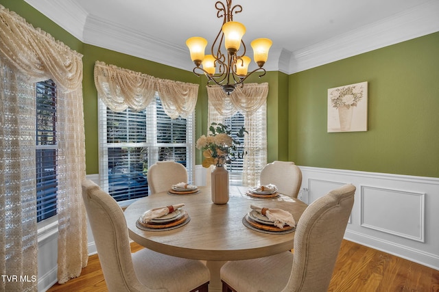 dining room featuring wood finished floors, wainscoting, crown molding, and an inviting chandelier