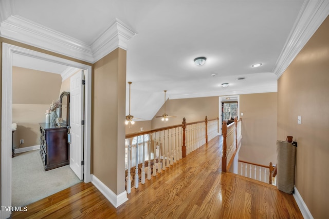 hallway featuring light wood finished floors, ornamental molding, vaulted ceiling, and an upstairs landing