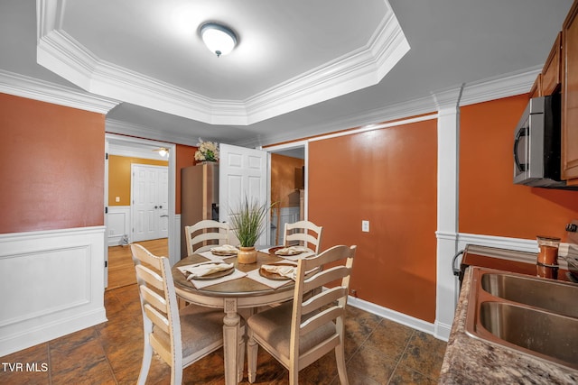 dining space with a decorative wall, wainscoting, a raised ceiling, and crown molding