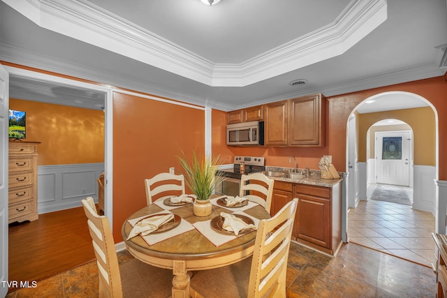 dining space with visible vents, arched walkways, a raised ceiling, and wainscoting