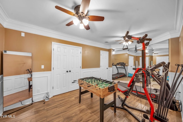 rec room featuring a ceiling fan, ornamental molding, wood finished floors, and wainscoting