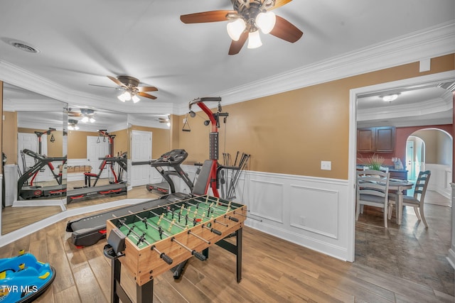 game room featuring a wainscoted wall, arched walkways, wood finished floors, and ornamental molding