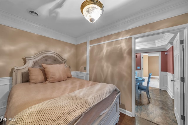 bedroom with a wainscoted wall, visible vents, a decorative wall, ornamental molding, and dark wood-type flooring