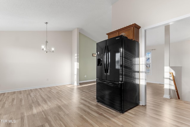 kitchen with lofted ceiling, black fridge, a chandelier, hanging light fixtures, and light hardwood / wood-style flooring