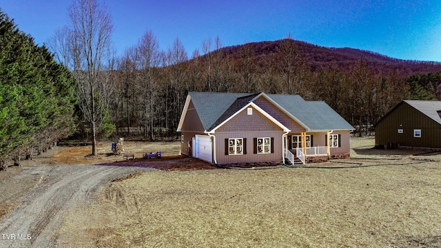 view of front facade featuring a garage, a porch, a view of trees, and dirt driveway