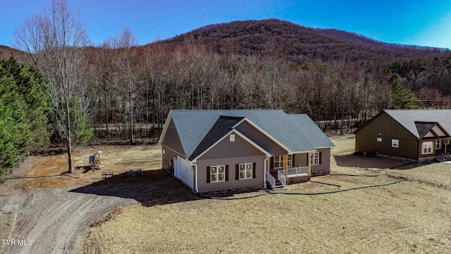 exterior space with a porch, dirt driveway, a wooded view, and a mountain view