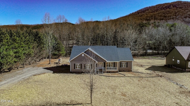 view of front of home with dirt driveway, a porch, and a wooded view