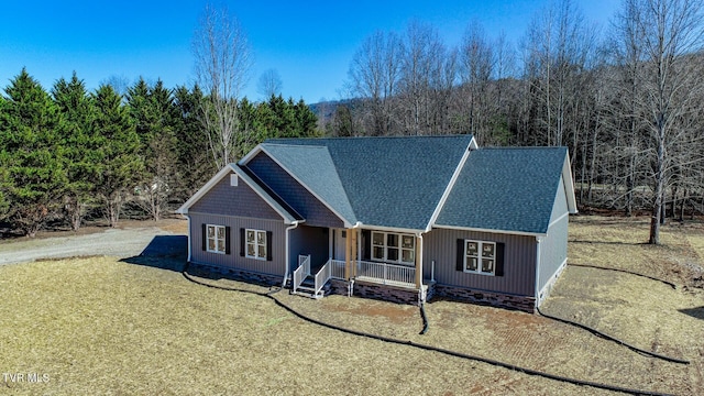 view of front facade featuring a shingled roof, covered porch, dirt driveway, and a front lawn