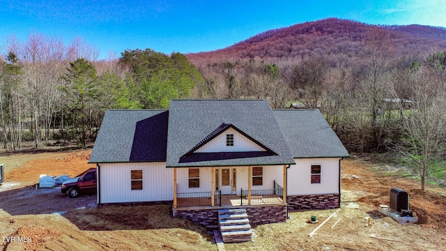 modern farmhouse featuring covered porch, roof with shingles, a mountain view, and a forest view