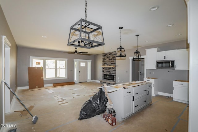 kitchen with white cabinets, stainless steel microwave, open floor plan, hanging light fixtures, and a stone fireplace