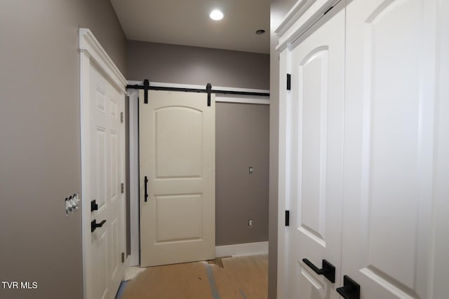 corridor featuring a barn door, baseboards, and recessed lighting