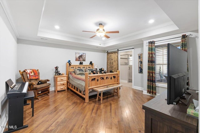 bedroom with ornamental molding, a raised ceiling, ceiling fan, a barn door, and light hardwood / wood-style floors