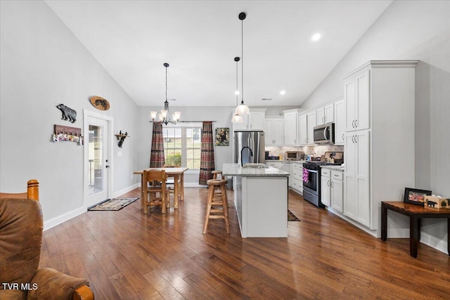 kitchen featuring appliances with stainless steel finishes, white cabinetry, a kitchen bar, light stone countertops, and a center island with sink