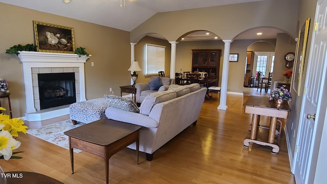 living room with vaulted ceiling, a tiled fireplace, decorative columns, and light hardwood / wood-style flooring