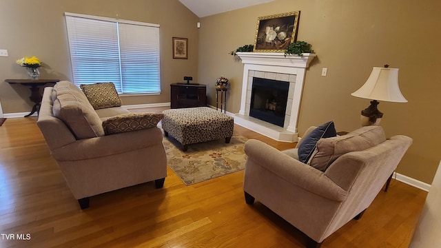 living room with a tile fireplace, vaulted ceiling, and hardwood / wood-style floors