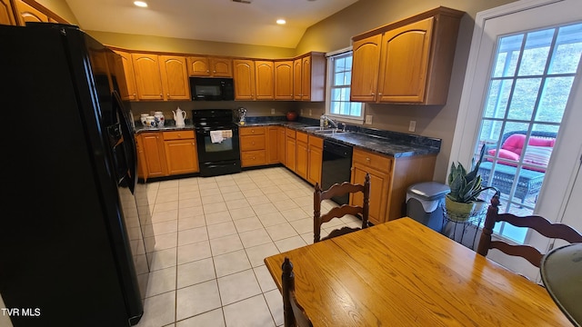 kitchen featuring lofted ceiling, sink, light tile patterned floors, dark stone counters, and black appliances