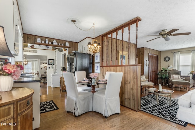 dining room with ceiling fan with notable chandelier, wooden walls, wood finished floors, and a textured ceiling