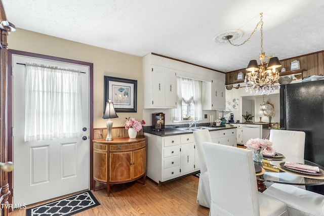 kitchen with dark countertops, a chandelier, white cabinets, and white dishwasher