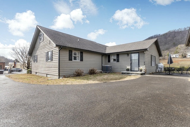 ranch-style house featuring central AC unit, a shingled roof, and a patio