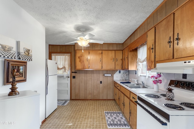 kitchen featuring white appliances, wooden walls, a sink, light countertops, and under cabinet range hood