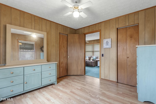 unfurnished bedroom featuring wooden walls, a textured ceiling, light wood-style floors, and multiple closets