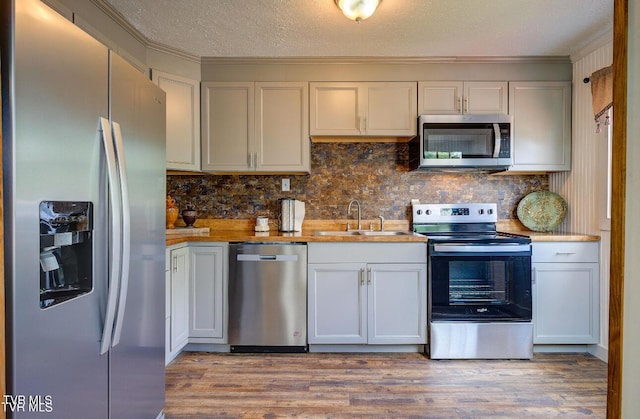 kitchen featuring sink, white cabinetry, light wood-type flooring, stainless steel appliances, and decorative backsplash