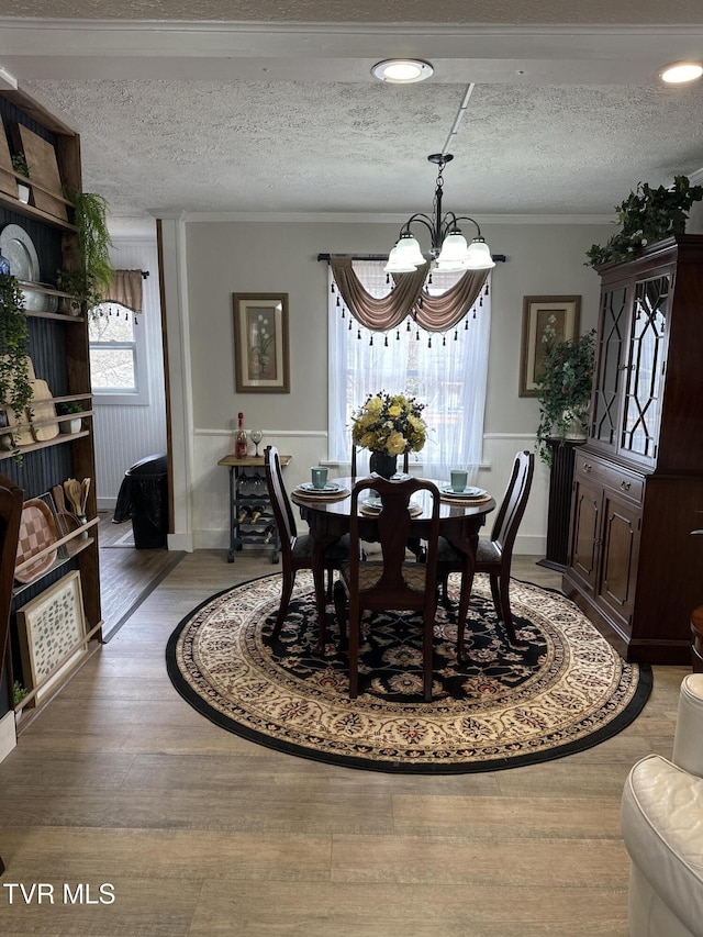 dining room featuring wood-type flooring, crown molding, a textured ceiling, and a chandelier