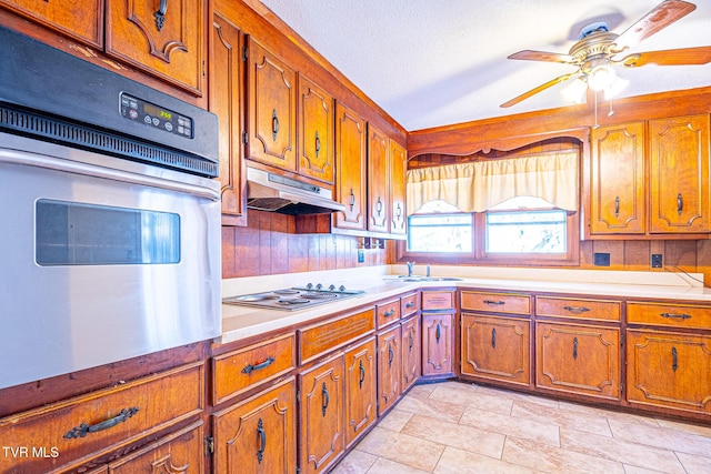 kitchen featuring cooktop, sink, a textured ceiling, ceiling fan, and oven