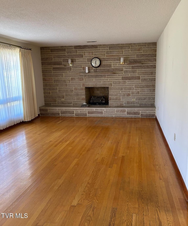 unfurnished living room featuring hardwood / wood-style flooring, a stone fireplace, and a textured ceiling