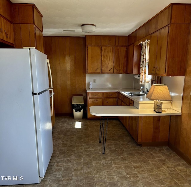 kitchen featuring wooden walls, kitchen peninsula, sink, and white fridge