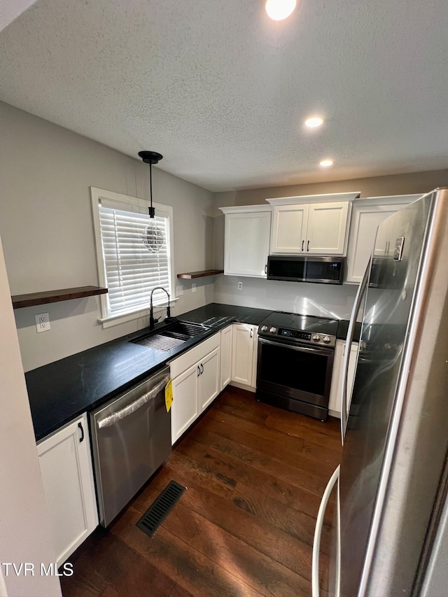 kitchen with dark wood-type flooring, sink, white cabinetry, appliances with stainless steel finishes, and pendant lighting