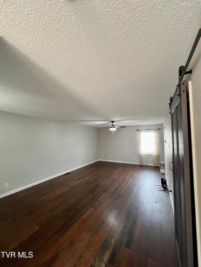 unfurnished living room with a textured ceiling, dark hardwood / wood-style floors, ceiling fan, and a barn door