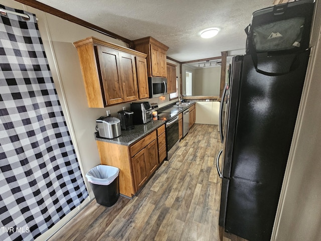 kitchen with dark wood-type flooring, appliances with stainless steel finishes, dark stone countertops, ornamental molding, and a textured ceiling