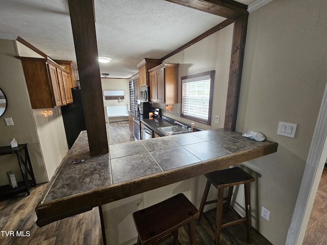 kitchen with sink, ornamental molding, tile counters, stainless steel appliances, and a textured ceiling