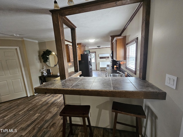 kitchen with black fridge with ice dispenser, tile countertops, kitchen peninsula, and a kitchen bar