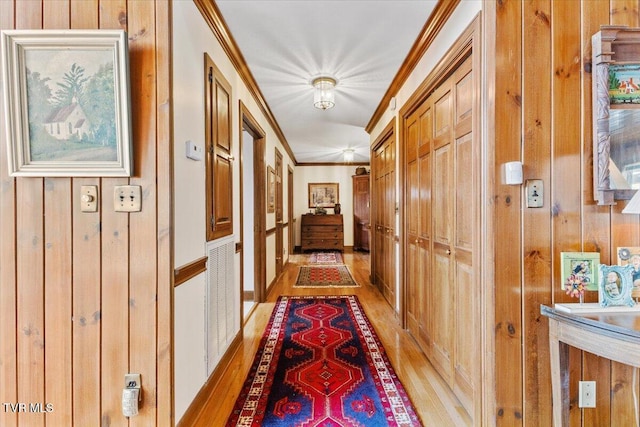 corridor with ornamental molding, wooden walls, and light hardwood / wood-style flooring