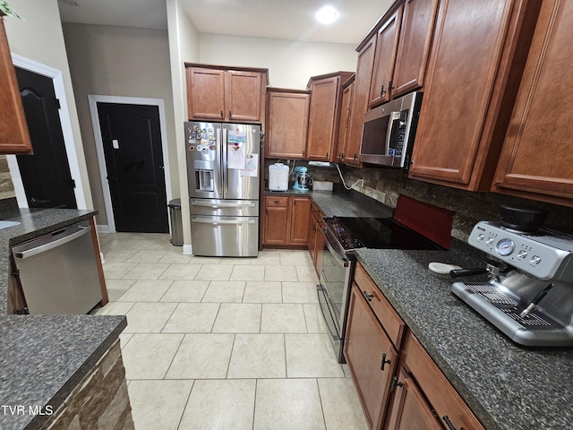 kitchen featuring dark stone countertops, backsplash, stainless steel appliances, and light tile patterned flooring