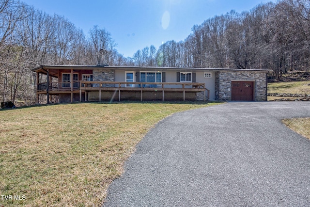 single story home with aphalt driveway, an attached garage, a front yard, stone siding, and a forest view