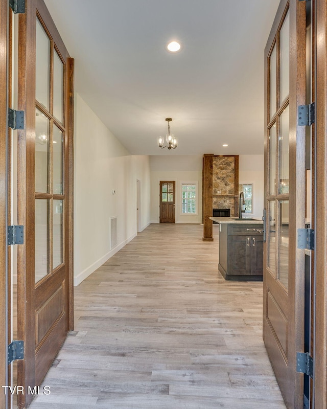 interior space with a chandelier, a sink, visible vents, baseboards, and light wood-type flooring