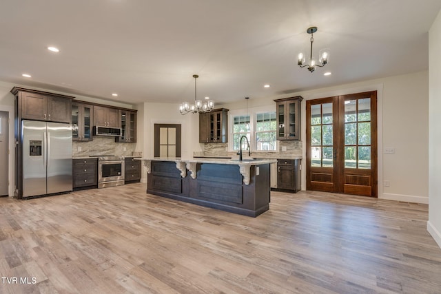 kitchen featuring glass insert cabinets, decorative light fixtures, stainless steel appliances, dark brown cabinets, and light countertops