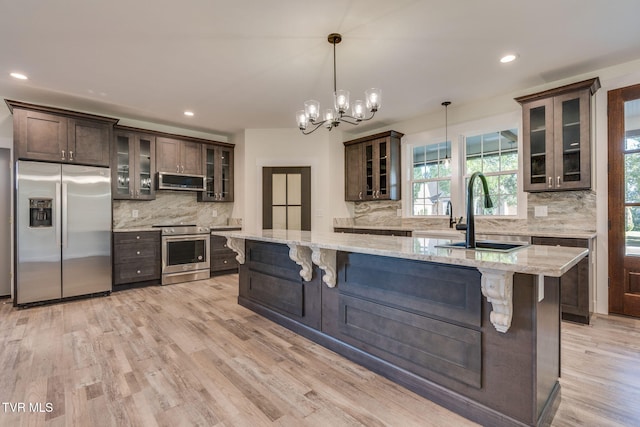 kitchen featuring stainless steel appliances, hanging light fixtures, glass insert cabinets, a sink, and light stone countertops