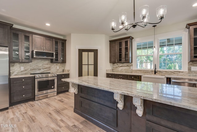 kitchen featuring appliances with stainless steel finishes, pendant lighting, glass insert cabinets, and extractor fan