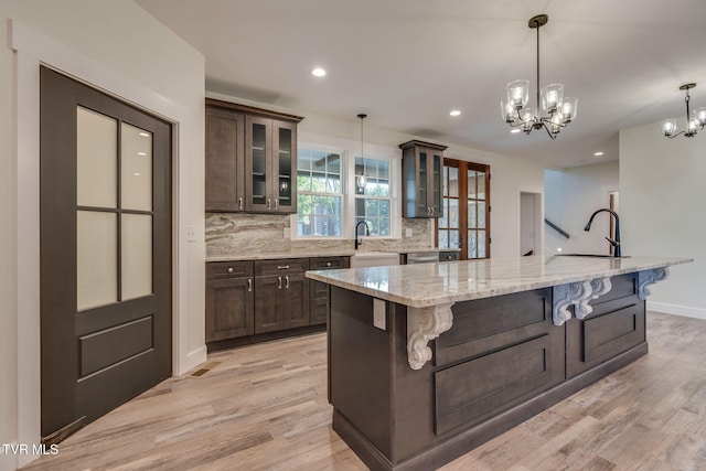 kitchen with a spacious island, a breakfast bar area, glass insert cabinets, light stone counters, and dark brown cabinets