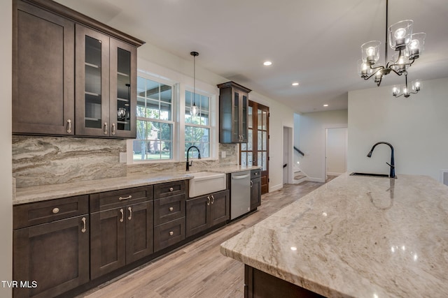 kitchen featuring glass insert cabinets, a sink, hanging light fixtures, and dishwasher