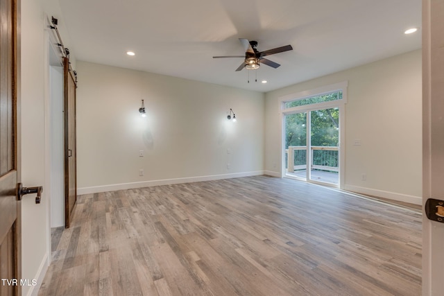 spare room with light wood-style floors, a barn door, baseboards, and a ceiling fan