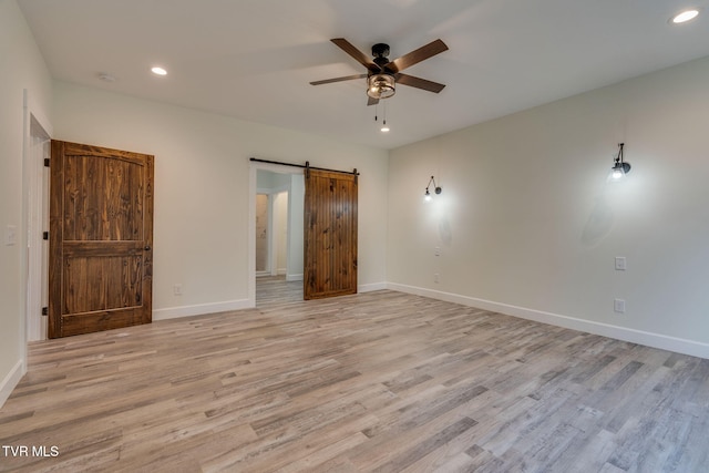 unfurnished bedroom with light wood-type flooring, recessed lighting, baseboards, and a barn door