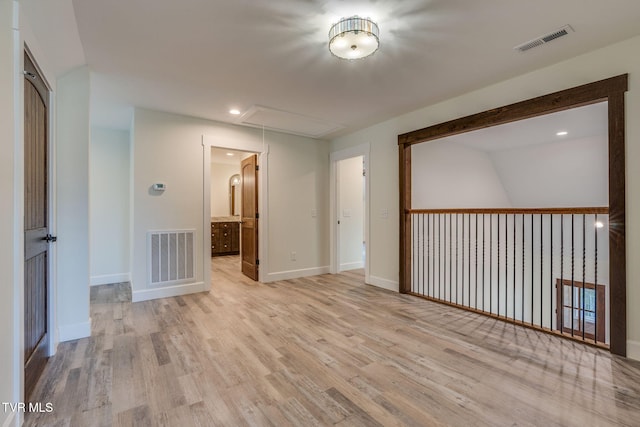 unfurnished room with baseboards, light wood-style flooring, visible vents, and attic access