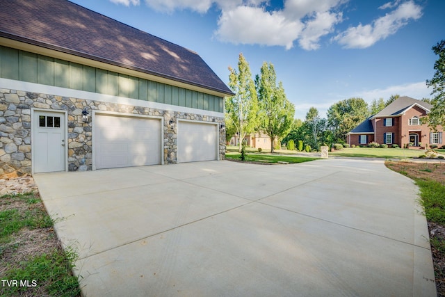 view of property exterior with a garage, driveway, board and batten siding, and stone siding