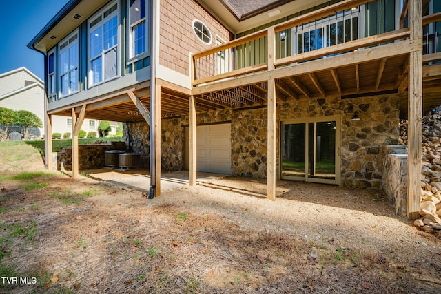 back of property with cooling unit, stone siding, and an attached garage